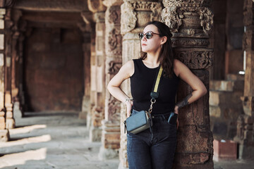 Attractive east asian woman in black sunglasses and black clothes stands among ancient pillars with...