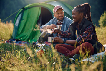 Happy black woman having cup of tea while camping with boyfriend in nature.