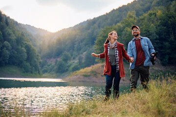 Carefree couple holding hands while walking by water in nature.