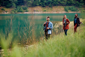 Young backpackers walking by lake in nature.