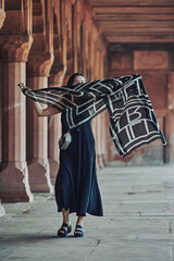 Fototapeta na wymiar East asian woman in black dress dancing with translucent scarf among columns of ancient indian temple, touristic walking in Taj Mahal of attractive happy young girl, joyful tourism in India