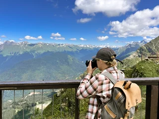 Tuinposter young stylish photographer woman taking photo of mountains standing at scenic viewpoint at Rosa peak, Sochi, Russia © Yulia Raneva