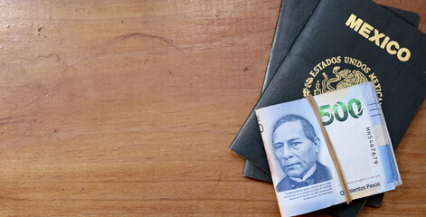 Mexican passport with a stack of Mexican banknotes on a wooden background, copy space.