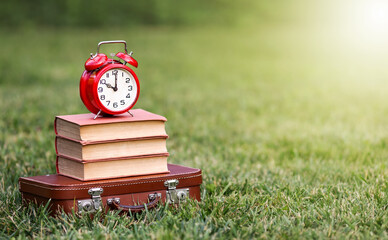 Vintage alarm clock on a retro schoolbag and books, back to school background