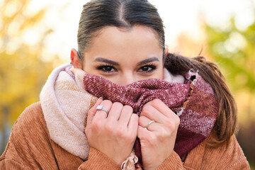 Caucasian young woman warming up her neck with a scarf during a cold autumn.