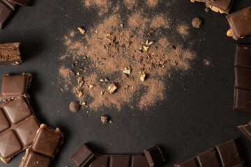 Chocolate on a black background with pieces and cocoa in the center. Copyspace.