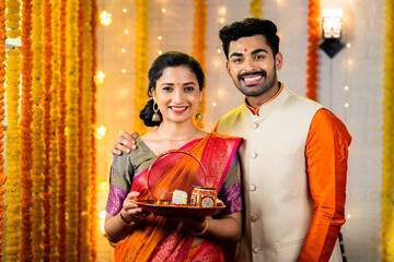 Portrait shot of happy smiling couple standing by holding karva Chauth plate set during festival...