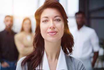 Portrait of a young woman standing in an office with colleagues in the background.