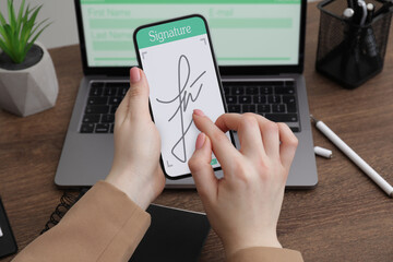 Electronic signature. Woman using mobile phone at wooden table, closeup