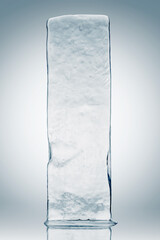 Crystal clear, pure ice block, on white surface with reflection. Rectangular piece of ice.