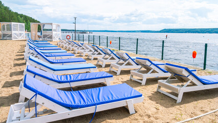 Deck chairs with throw mattresses for relaxing on the beach. Relaxing on the beach by the sea.  Summer tan by the water. A relaxation area with sun loungers on the sandy beach for sunbathing.
