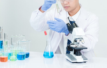 Man asian student scientist Wearing a doctor's gown in the lab looking at the chemist. caused by mixing reagents in scientific research laboratories with test tubes and microscope on the table