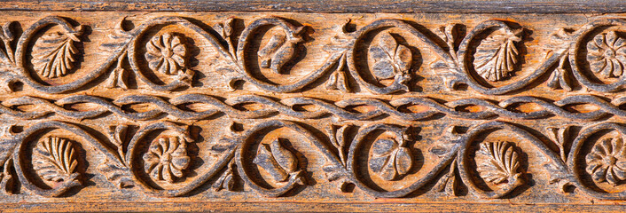 A close-up with a wooden sculpture with floral motifs . The pillars of the traditional gates are...