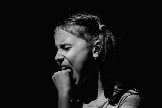 Lost childhood and children's pain concept. Psychological portrait of sad unhappy young girl biting her fist as a symbol of feeling of helplessness and despair. Black and white image.