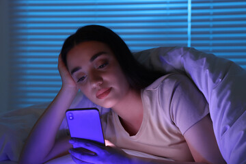 Young woman using modern smartphone in bed at night. Internet addiction