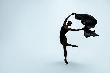 Beautiful ballerina with black veil dancing on light background, space for text. Dark silhouette of...