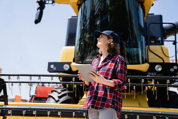 Woman farmer with digital tablet on a background of harvester. Smart farming concept