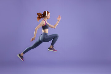 Fototapeta na wymiar Woman in sportswear jumping on violet background, space for text