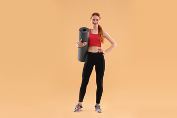 Fototapeta na wymiar Young woman in sportswear with fitness mat on beige background