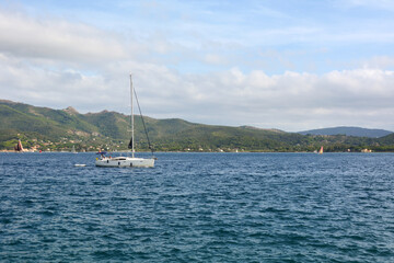 A sea pleasure sailing yacht sails across the sea to the left. A mountain coast in the distance. A...