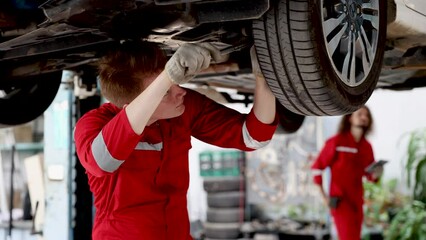 Attractive Caucasian mechanics man fix wheels by wrench underneath damage car, technician male concentrate job repair services, worker in uniform working in garage, small business auto car maintenance