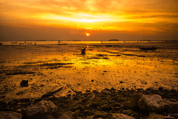 Fototapeta na wymiar dramatic sky during sunset with rocks and boats foreground in Bangkalan, Madura, Indonesia.