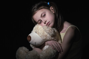 Lost childhood, emotional pain,  and children's pain, depression and domestic violence concept. Psychological portrait of sad unhappy young girl hugs her friend teddy bear toy.