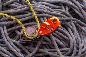 assisted breaking belay device with rope threaded through, on a background of flaked climbing rope
