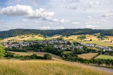Fototapeta na wymiar Aerial view of German countryside with small village among farmland, green leafy trees covering hill in background, sunny day in Eiffel Kreis, Bitburg-Prüm district in Rijnland-Palts, Germany