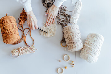 Macrame leaf in natural color. Top view of woman creating macrame on white table. Female hands...
