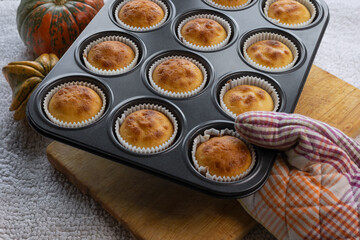 Close up female hand holding iron mold with homemade pumpkin muffins. Autumn dessert and recipes. 