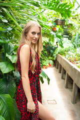 Glamorous blonde model in stylish black swimsuit and transparent robe posing in lush green tropical...