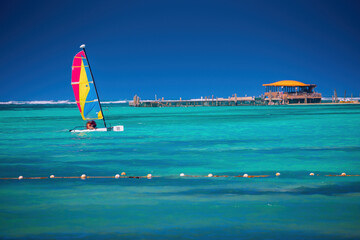 Color catamaran sailboat or winsurf sailing in calm caribbean sea, summer vacation and sport