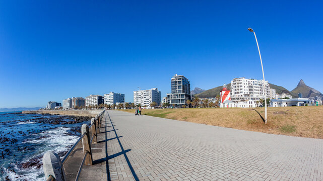 Cape Town Sea Point Promenade along Atlantic Ocean shoreline with Apartments and Table Mountain Lions Head in blue sky.
