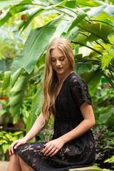 Beautiful woman in black summer dress on jungle leaves tropical background
