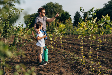 Side view of a Caucasian man standing in the orchard with his son and talking to him.