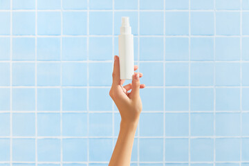 Womans hand holding white tube on blue tile background. Beauty treatment. Skin care routine
