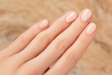 Beautiful womans hand with nude nail design on beige background. Manicure, pedicure beauty salon concept