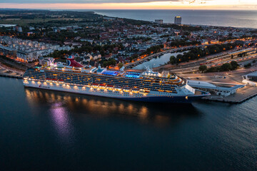Rostock, Warnemuende, Germany,  aerial dusk view of illuminated cruise ship "Carnival Pride" of Carnival Cruise Line, moored at Cruise Ship Terminal, Warnemuende city in the background 