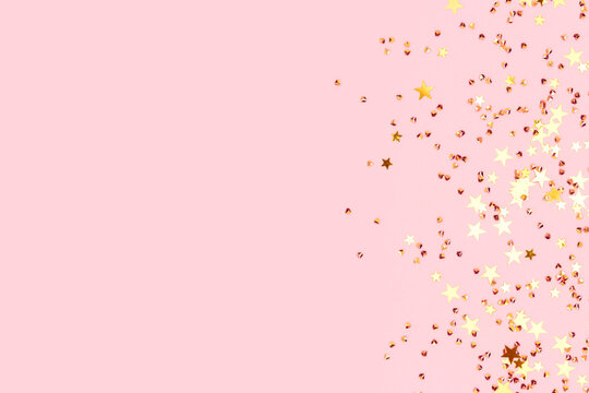 Glowing gold colored stars and crystals confetti on a pink background. Festive concept with place for text. Selective focus.