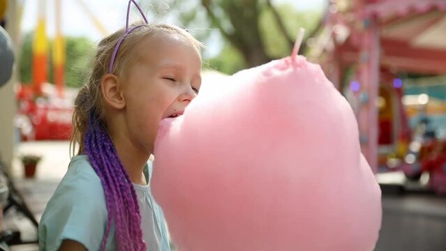 happy baby girl eating cotton candy at amusement Park in summer