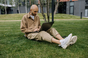 Young entrepreneur student freelance tutor using laptop for remote remote work, checking email, e-banking online, sitting on green grass lawn