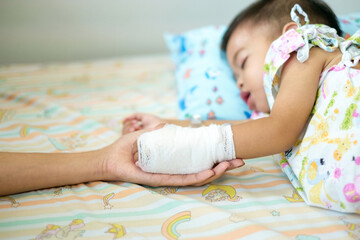 A 1.5-year-old Asian boy is sick and is being treated at the hospital. A mother's hand is holding her wrapped son's hand.