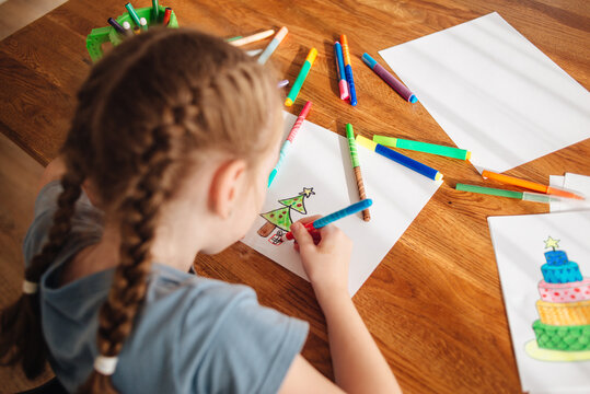 The child spends time creating and drawing. A girl draws a Christmas tree with felt-tip pens