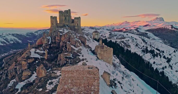 Aerial view of the Rocca di Calascio with snow and illuminated by the light of the sunset, behind the chain of the Gran Sasso and the Corno grande. Gran Sasso and Monti della Laga National Park, Abruz