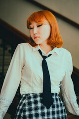 A beautiful ginger Asian schoolgirl in a white shirt and black tie stands poised in school, exuding...