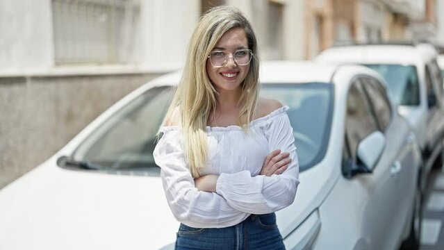 Young blonde woman standing with arms crossed gesture leaning on car at street