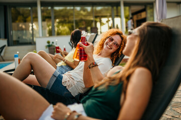 The friends arrange colorful pool floats, umbrellas, and lounge chairs, creating a vibrant and...