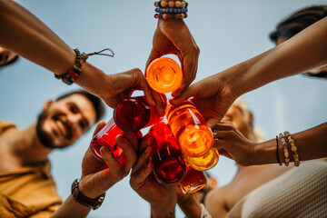 Low angle view of a group of people with their cocktail bottles in a toast, clinking them together and expressing their excitement for the upcoming celebration.