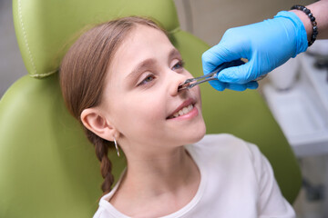 Specialist otolaryngologist in protective gloves examines the childs nose